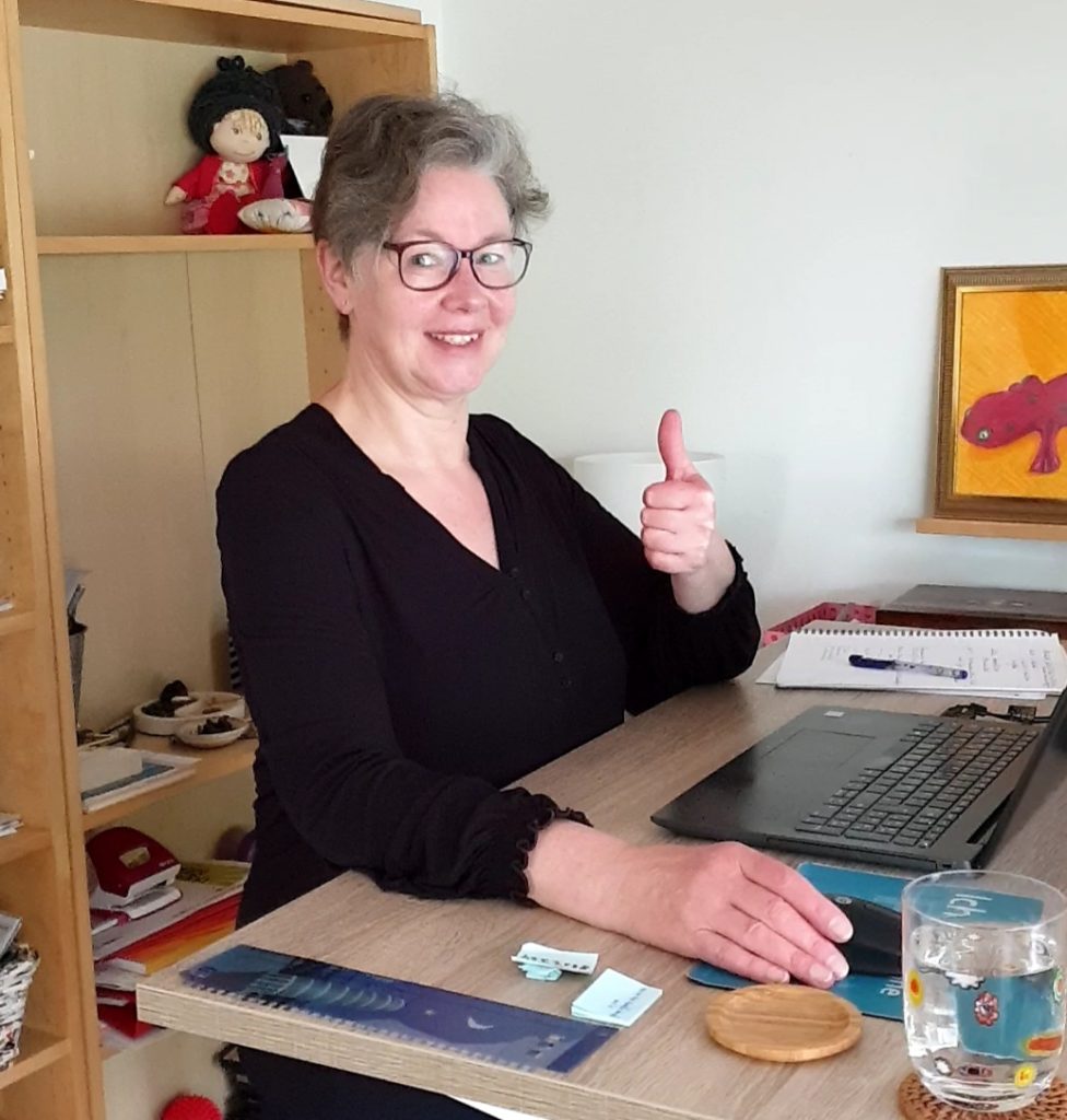 Silke Geissen sitzt an ihrem ordentlichen Schreibtisch und zeigt strahlend ein "Daumen hoch"