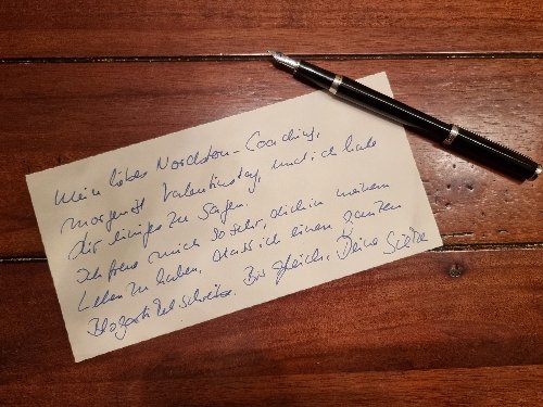 Eine handgeschriebene Briefkarte als Symbol für einen Liebesbrief an das Business der Autorin liegt auf einem Holztisch, daneben ein offener Füller.