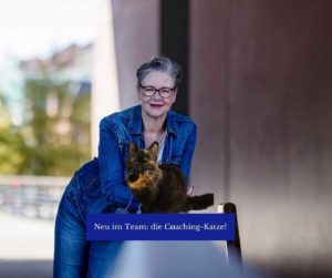 Die Autorin lehnt an einem Geländer, vor ihr ins Bild montiert sitzt eine Katze