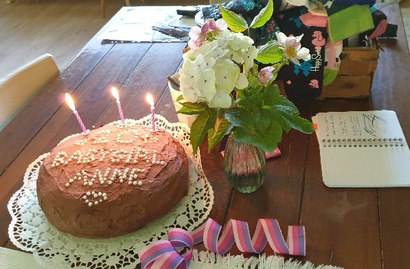 Ein Geburtstagstisch mit Blume in einer Vase, Geburtstagskuchen mit Aufschrift "Babygirl Anne 20", Luftschlangen, Kerzen und Geschenke