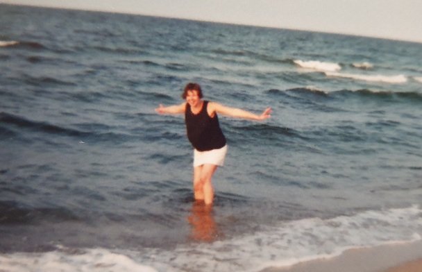 Einer meiner besten Tipps für heiße Tage: Wasser! Im Bild: Die Autorin in sehr jungen Jahren bewegt sich, als würde sie fliegen. Die Beine im Meer, die Arme ausgestreckt.
