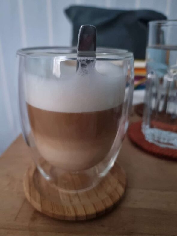 Ein Cappuccino in einem doppelwandigen Glas. Es zeichnen sich viele Schichten ab von unvermischtem Kaffee, unvermischter Milch und verschiedenen Stufen der Durchmischung beider Flüssigkeiten.