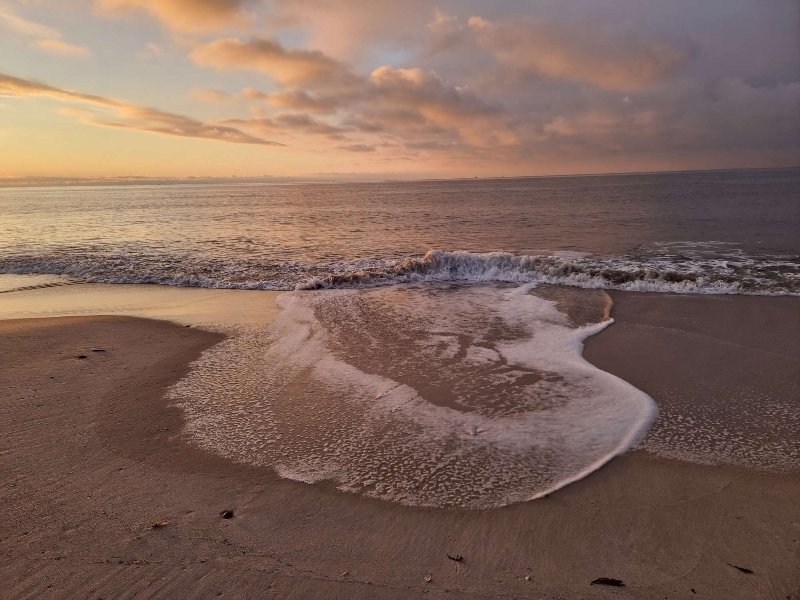 Winterliches Sonnenuntergangslicht am menschenleeren Strand mit einer großen flachen Welle am Sandstrand