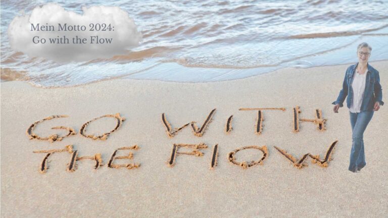 Ein Sandstrand am Meer. In einer Wolke der Text: Mein Motto 2024: Go with the Flow. Der Text ist auch noch einmal in den Sand geschrieben. Neben dem Schriftzug im Sand geht die Autorin.