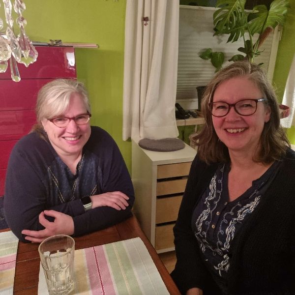 Silke Geissen und Britta Hohne sitzen am Tisch über Eck und lachen gemeinsam.