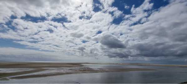 Wattenmeer bei auflaufendem Wasser, darüber endloser Himmel mit weißen Wolken