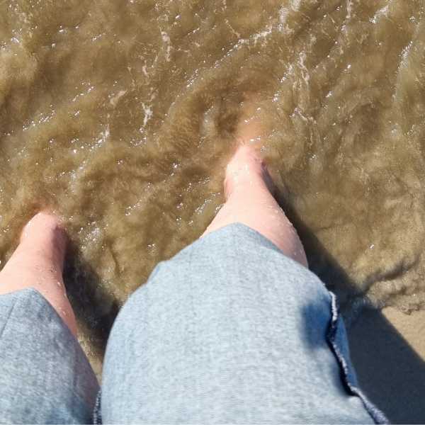 Nackte Füße in trübem, sprudeligem Wasser, unter einer hochgerollten Jeans.