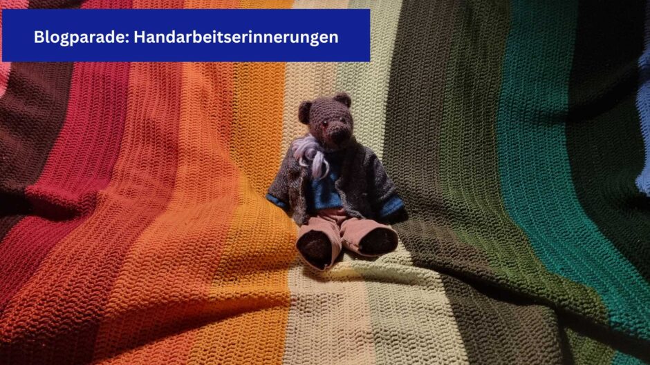 Auf einer bunten gehäkelten Wolldecke sitzt ein brauner, ebenfalls gehäkelter Teddy in Cordhose, Pullover und Jackett.