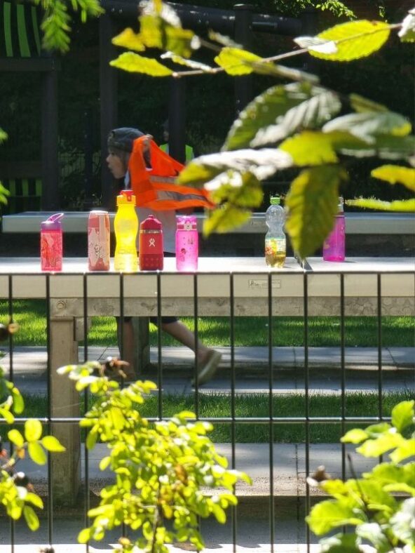 Auf einem Spielplatz stehen bunte Kindertrinkflaschen in der prallen Sonne auf einer Tischtennisplatte.