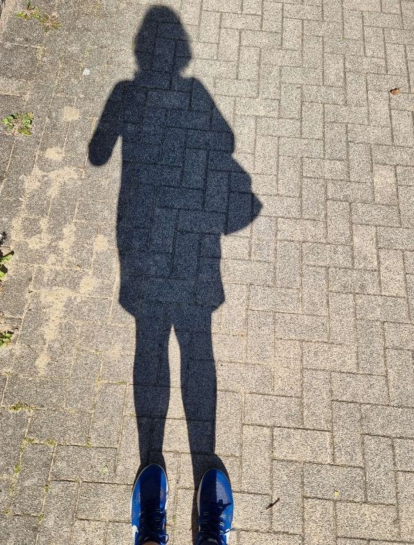 Der Schatten der Autorin auf Pflastersteinen, im unteren Bildrand die blauen Sportschuhe.