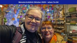 Vor einem glitzernden Hintergrund in einem Deko-Laden stehen zwei Frauen, die Autorin Silke Geissen und Umani Wendler, und lächeln. Oben im Bild ein blaues Banner mit weißem Text: Monatsrückblick Oktober 2025 – when I’m 64