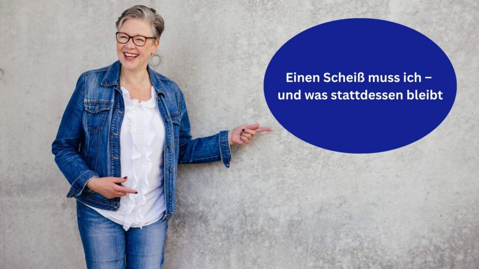 Die Autorin steht lachend vor einer Betonwand und zeigt auf ein blaues Schild mit weißer Aufschrift: Einen Scheiß muss ich – und was stattdessen bleibt