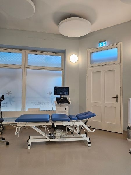 Ein Behandlungsraum in der Orthopädiepraxis. Satinierte Fenster, eine Altbautür, eine Behandlungsliege, diverse Instrumente.
