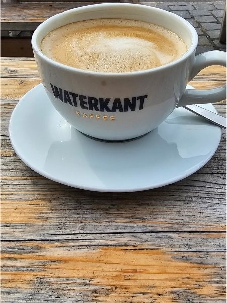 Eine Tasse Cappuccino auf einem verwitterten Holztisch, der zu einem Café an der Elbe gehört.